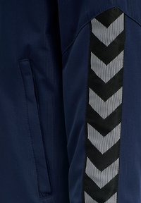 Giacca navy con tessuto testurizzato, tasca laterale e una striscia a zigzag bianca e nera lungo la manica.