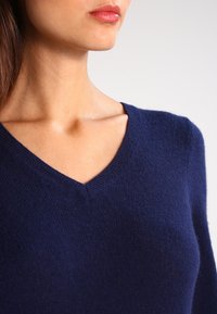Pull en maille douce bleu marine avec un col en V. Présente une coupe ajustée et une texture fine, adapté au superposition ou à un port décontracté.