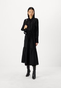 Mustapaitainen pitkähihaisia mekko, jossa on solmittava vyötärö, kerroksellinen helma ja pistekuvio. Yhdistetty polvenyskäisiin mustiin saappaisiin ja pieneen mustaan käsilaukkuun.