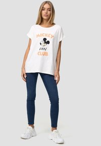 Witte katoenen T-shirt met korte mouwen, voorzien van een zwart-wit Mickey Mouse graphic en de tekst "FAN CLUB" in perzik, gecombineerd met blauwe jeans.