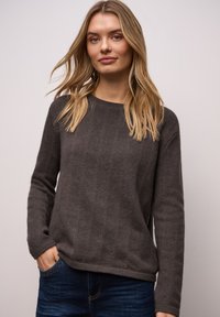 Grauer Strickpullover mit lockerem Sitz, langärmlig, mit Rundhalsausschnitt und strukturierter Oberfläche. Kombiniert mit dunkelblauen Jeans.