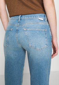 Jeans de mezclilla azul claro con corte recto, que cuentan con dos bolsillos traseros, un desgastado sutil y costuras amarillas a lo largo de las costuras.