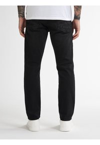 Zwarte denim jeans met een rechte snit, subtiele structuur en achterzakken. Gecombineerd met witte sneakers, wat een casual stijl uitstraalt.