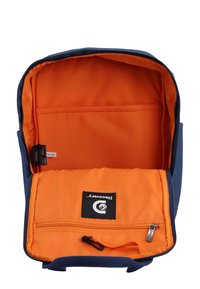 Zaino blu navy con un interno arancione, dotato di una tasca con zip e un'etichetta con logo. L'interno ha una texture liscia e un design elegante.