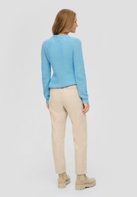 Hellblauer gestrickter Pullover mit strukturiertem Rippmuster, kombiniert mit beigen maßgeschneiderten Hosen und beigen Knöchelstiefeln, die ein schlankes Design aufweisen.