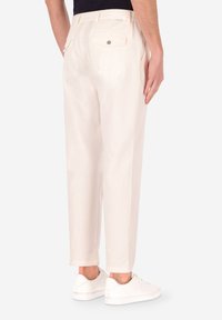 Pantaloni beige chiaro con una vestibilità comoda, dotati di tasche posteriori, una texture sottile e una cintura liscia, abbinati a sneakers bianche.