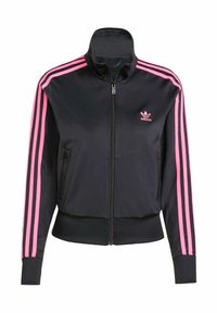 Giacca nera Adidas con zip, strisce rosa lungo le maniche e piccolo logo Adidas rosa sul petto, dotata di tasche laterali con zip.