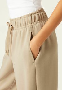 Beiga, mjuka joggers i tyg med elastisk midja, snörningsdetalj och sidofickor. Slät textur med en avslappnad passform.