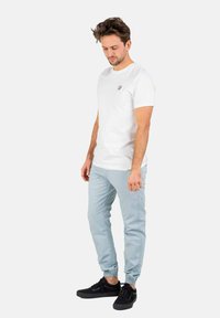 Camiseta de algodón blanca con un pequeño logo negro, combinada con pantalones jogger azul claro con puños elásticos y zapatillas negras.