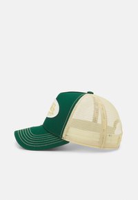 Casquette en tissu vert avec un dos en mesh beige, visière courbée et un logo circulaire blanc à l'avant, comportant des lettres et des accents jaunes.