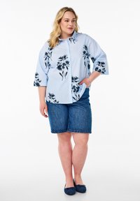 Camicia azzurra chiara con stampa floreale nera, abbinata a shorts di jeans. La camicia ha un colletto e maniche a tre quarti, ed è dotata di una tasca.