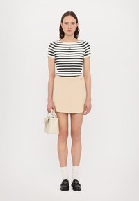 Sort-hvid stribet ribbet t-shirt, beige indpakningsskørt med knapdetalje, hvid håndtaske, hvide sokker og sorte loafers.