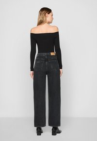 Svart off-shoulder långärmad topp som matchas med hög midja, vida svarta jeans. Noterbara detaljer inkluderar klassiska bakfickor och en tan etikett.