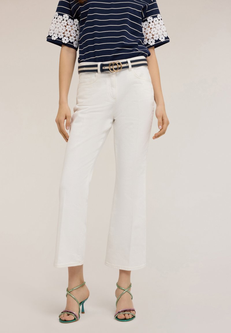 Pantalones de pierna ancha blancos combinados con una blusa a rayas azul marino con acentos de encaje floral blanco; complementados con tacones verdes con tiras.