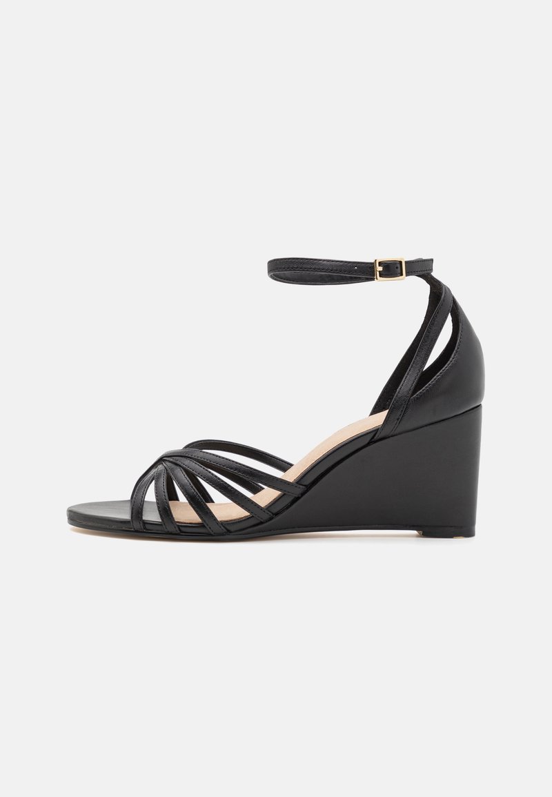 Sandale compensée noire avec plusieurs fines lanières sur les orteils, bride à la cheville avec boucle dorée, et contrefort fermé au talon.
