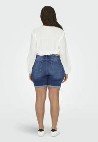 Balta ilgomis rankovėmis bliuska su tekstūruotu audiniu, derinama su tamsiai mėlynomis džinsiniais šortais su apverstais kraštais ir užpakalinėmis kišenėmis. Balti sportiniai bateliai užbaigia aprangą.