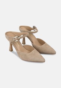 Tacones slingback de ante color beige con punta afilada y tacón de bloque de altura media. Presentan un acento decorativo de hebilla en la correa del tobillo.
