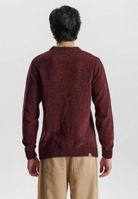 Bordeauxfarbener Strickpullover mit geripptem Kragen und Bündchen, ausgestattet mit einem strukturierten Stoff und einem kleinen Markenetikett an der unteren linken Seite.