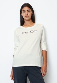 Langærmet, off-white t-shirt lavet af blødt stof, med rund halsudskæring og et sort logo, der står "Marc O'Polo EST. IN STOCKHOLM."