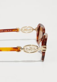 Ochelari de soare din tip tortoise cu o ramă groasă, având un accent auriu pe tâmple care reprezintă un design cu un cal și o trăsură.
