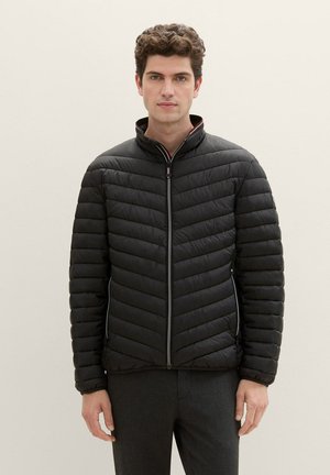 Schwarze Steppjacke mit einem Zickzack quiltierten Design, hohem Kragen, Reißverschluss und Seitentaschen, mit kontrastierenden Details innen.