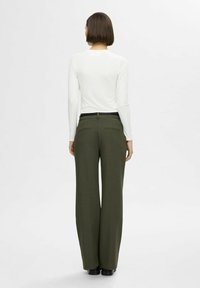 Witte lange mouwen shirt gecombineerd met hoog-geknoopte olijfgroene wijde broek, met twee achterzakken en een zwarte riem.