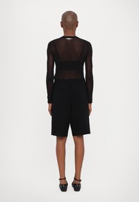 Černý průsvitný top s dlouhým rukávem a nastavovacími ramínky, doplněný černými šortkami ke kolenům a černými botami s dekorativními cvoky.