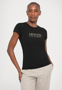 Tricou negru, ajustat, cu mâneci scurte, având un logo auriu "ARMANI EXCHANGE" pe față. Material din bumbac neted, design minimalist.