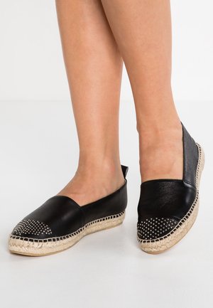 Mustat nahka-espadrillokset, joissa on teksturoitu kudottu juutti-pohja. Pyöreä kärki, jossa niittikoristeita edessä, avoimet sivut hengittävyyden vuoksi.