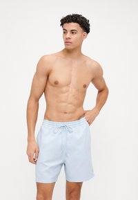 Shorts de bain bleu clair en tissu lisse, dotés d'une taille à cordon de serrage et d'un petit logo doré sur le côté.