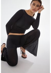 Zwart top met lange mouwen gecombineerd met wijde broekspijpen, beide in een geribbelde textuur. Eenvoudig ontwerp, aansluitende top en vloeiende broek met een zachte val.