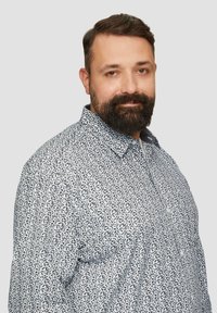 Koszula zapinana na guziki z białym tłem ozdobionym małymi czarnymi kwiatowymi wzorami, krótkim kołnierzykiem i delikatną teksturą. Zbliżenie na górną część ciała mężczyzny.