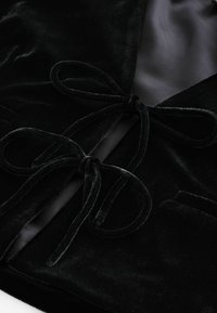 Gros plan sur un tissu en velours noir avec deux nœuds de ruban en velours noués sur un fond rayé gris.