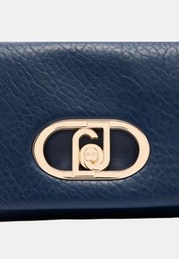 Borsa in pelle blu marino con texture, caratterizzata da una hardware ovale color oro con lettere intrecciate e un dettaglio circolare del logo.
