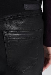 Pantalon en denim noir avec une coupe intermédiaire, des coutures visibles et une poche arrière avec une étiquette en cuir embossée portant "Sisley".