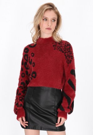 Maglione rosso peloso con stampa animale nera e motivi a righe sulle maniche, abbinato a una mini gonna nera in ecopelle.