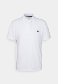 Polo blanc en coton, avec un col classique, un plastron à deux boutons, et un petit logo de crocodile vert sur la poitrine gauche.