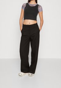 Černé kalhoty s rovnými nohavicemi, nošené s krátkým černým tílkem a světle fialovou vrstvenou košilí. Obuv tvoří stříbrné sportovní boty.