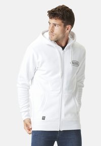 Haut à zip blanc en tissu polaire, avec un patch logo à l'avant, des poches kangourou et une capuche avec cordon.