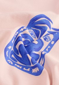 Textil que presenta una suave tela rosa con un gran diseño de cara abstracta azul, incorporando formas orgánicas y elementos decorativos.