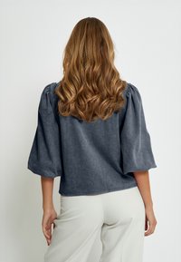 Graues Denim-Oberteil mit Puffärmeln und lässiger Passform. Weicher Stoff, runder Ausschnitt und sichtbare Nähte entlang dem Saum.