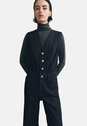 Vestido de peto de mezclilla negra con un escote en V profundo, botones plateados y bolsillos laterales. Diseño minimalista con detalles de costuras en contraste.