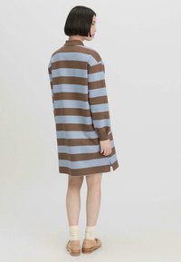 Gestreiftes Kleid in Braun und Hellblau, mit Kragen, langen Ärmeln und seitlichen Schlitzen. Der Stoff scheint weich und mit einem lässigen Schnitt zu sein.