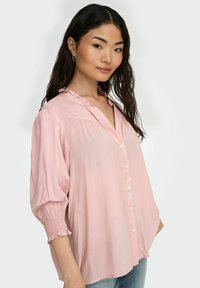 Lyserød bluse med rynkekrave, knaplukning foran og ballonærmer med smockede manchetter; lavet af et glat, letvægtsstof.