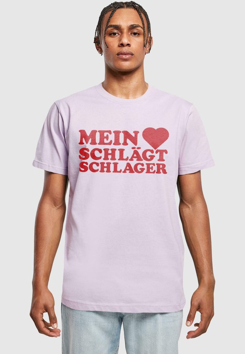 Lyserød bomulds T-shirt med fed rød tekst, der læser "MEIN ♥ SCHLÄGT SCHLAGER." Kortærmet og med klassisk crew neck design.