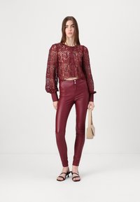 Bourgogne spetskort topp med långa puffärmar och knappstängning, i kombination med höga bourgognefärgade byxor i konstläder och svarta remsandaler.