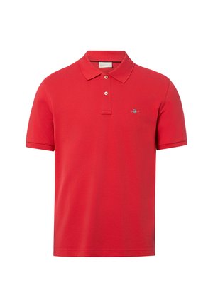 Polo rouge à manches courtes avec deux boutons et petit logo brodé sur la poitrine gauche, présenté sur un fond blanc uni.