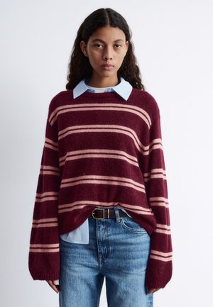 Burgundy striped sweater with pink stripes, knit texture, loose fit. Worn over a light blue collared shirt, paired with blue jeans and a black belt.