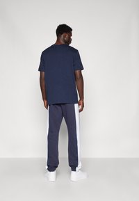 Camiseta de color azul marino con un ajuste relajado, combinada con joggers gris oscuro que tienen paneles laterales blancos. Zapatillas blancas completan el look.