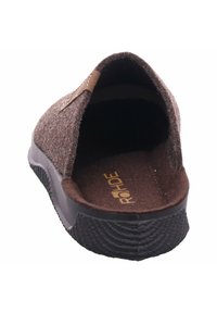 Zapato slipper de color marrón, hecho de fieltro, con una textura suave, forma redondeada y suela de goma. Presenta un logo en la plantilla y un acento cosido en la parte superior.